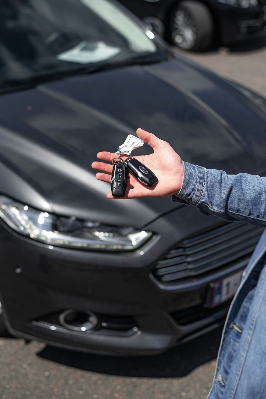 Hand met autosleutels voor een donkere Ford